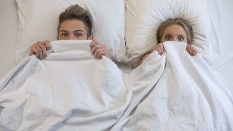 Couple in bed looking embarrassed.